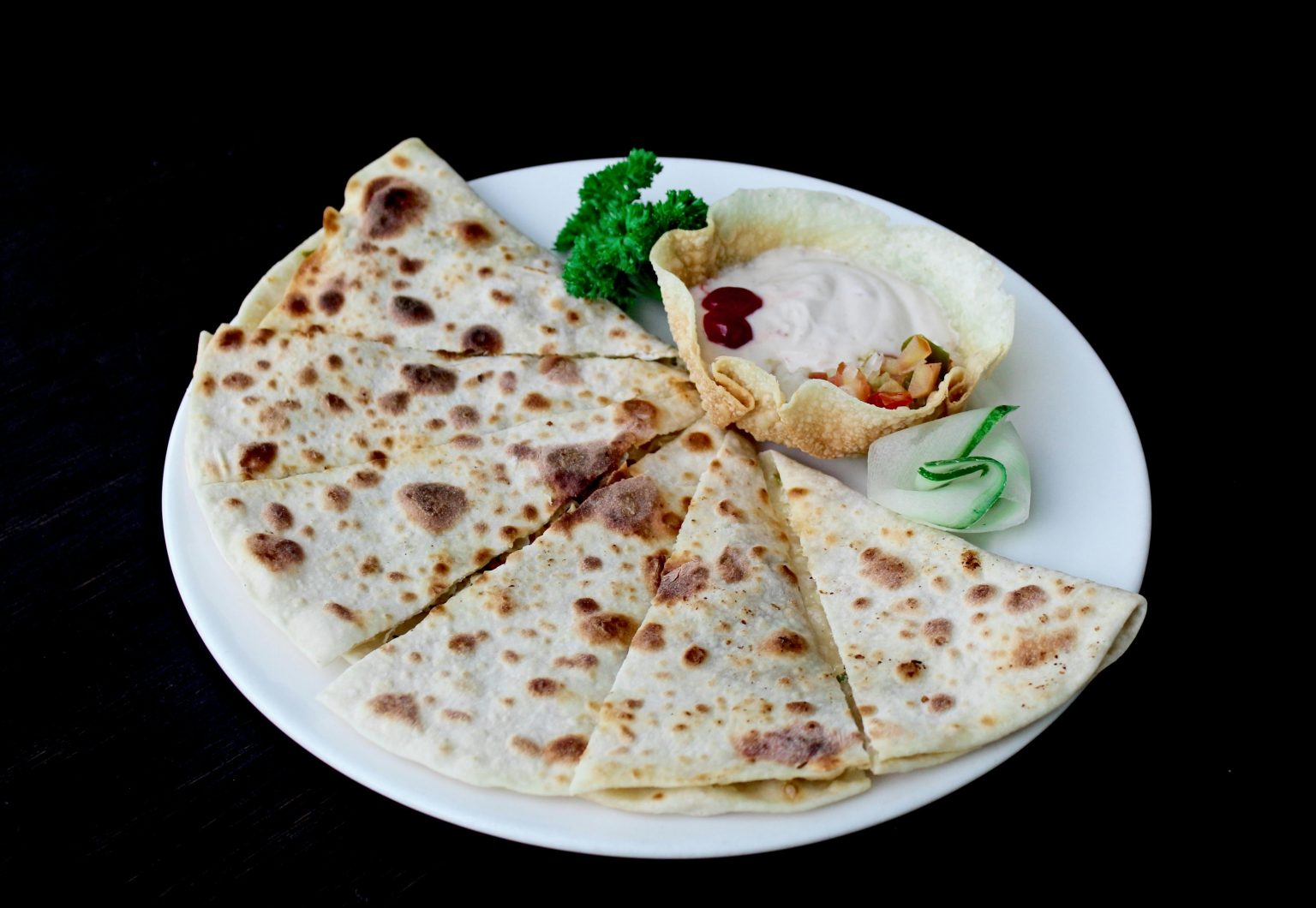 Close-up of a delicious quesadilla served with sauces and garnished on a plate, perfect for food photography.