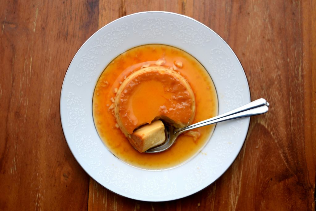 A delicious caramel flan dessert on a decorative plate with a spoon, top view.