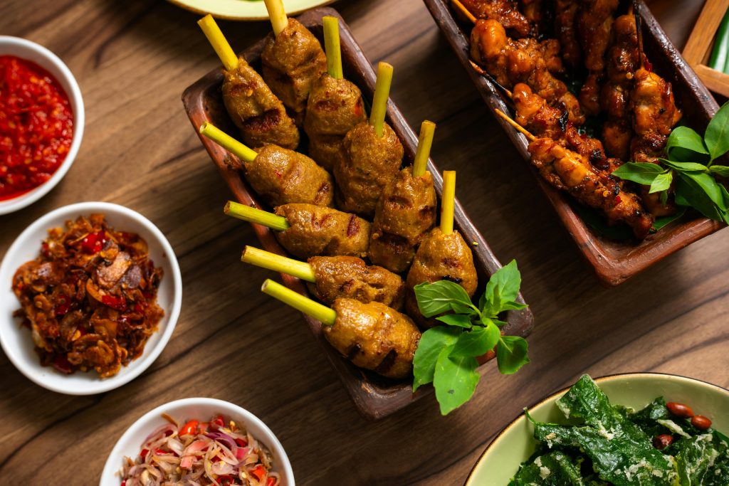A vibrant display of traditional Indonesian satay and sambal dishes on a rustic wooden table.