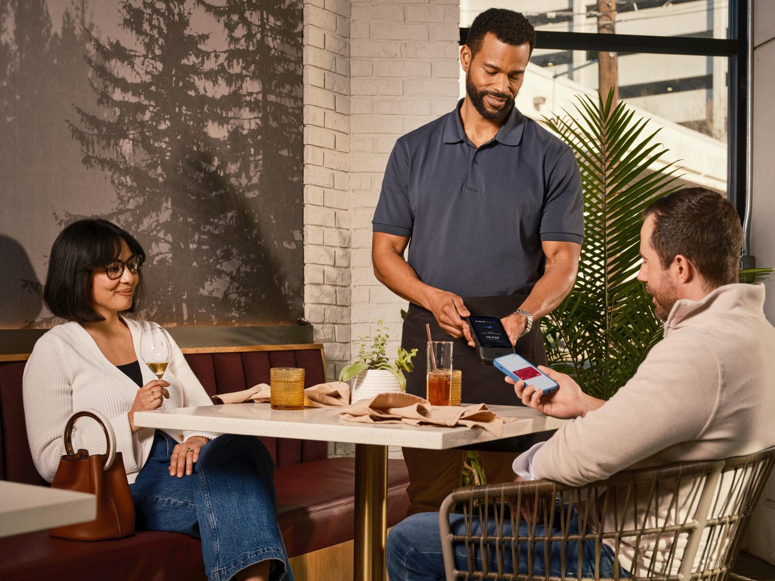 A customer uses mobile phone for contactless payment via handheld POS at a casual restaurant.