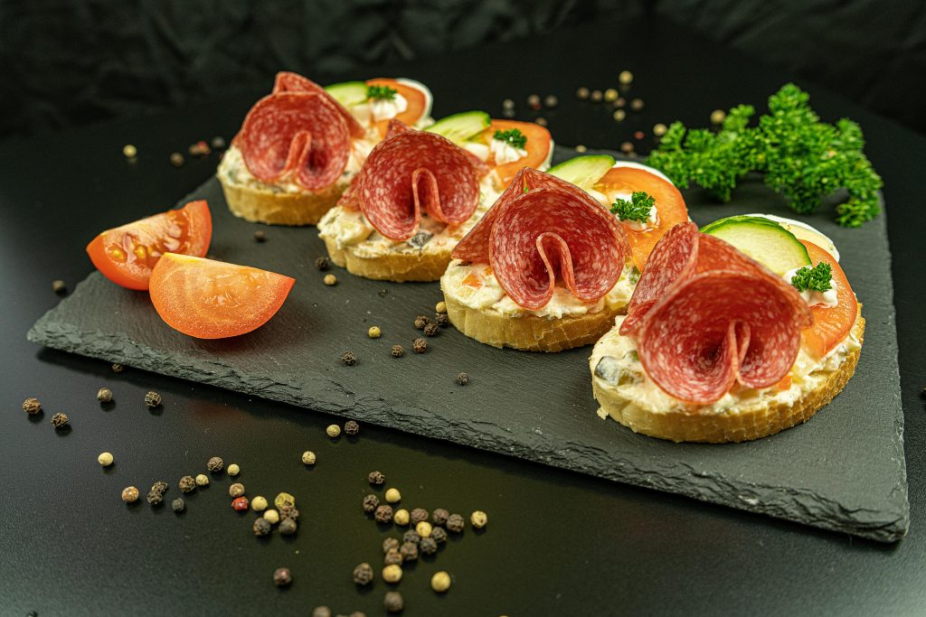 Tasty salami bruschetta served on a slate board with fresh vegetables and herbs.